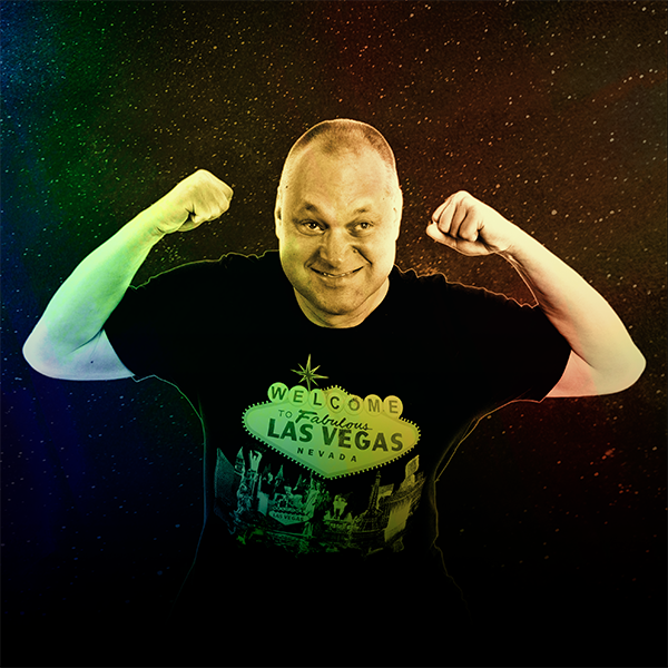 Late thirties light-skinned ensemble member, Mark Bedford, in a muscle-flex pose against a star background. The image is treated with a rainbow overlay to match the album artwork. Mark has buzzed brown hair, and is wearing a black “Welcome to fabulous Las Vegas” shirt.