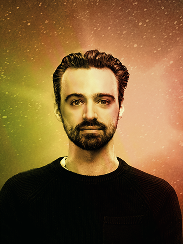 Clayton Smith. Clayton is in his mid-Thirties, wearing a black sweater, with black pushed-back hair, and a black trimmed beard. Image is treated with a rainbow overlay to match the album artwork.